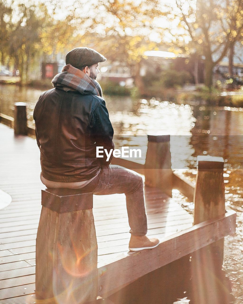 Rear view of thoughtful man sitting on wood by lake at public park