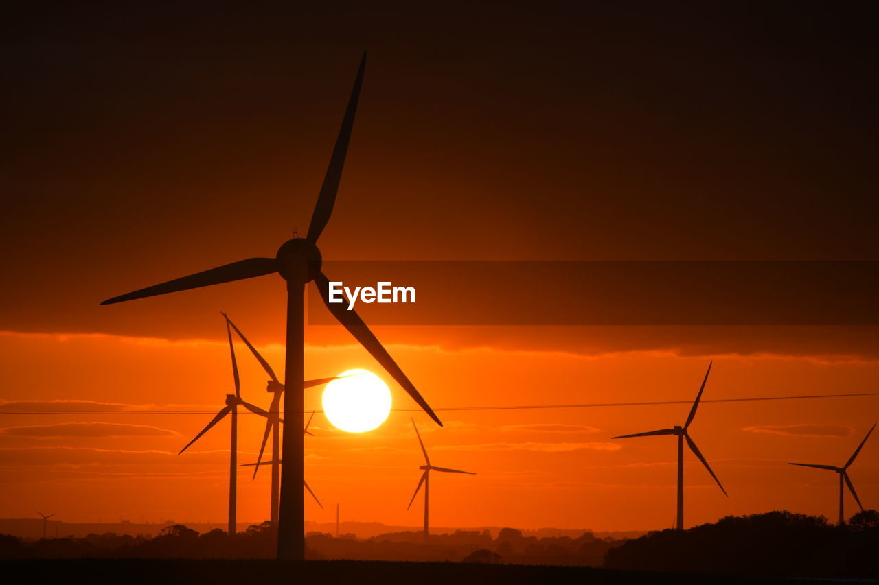 A bright red sunset through wind turbines