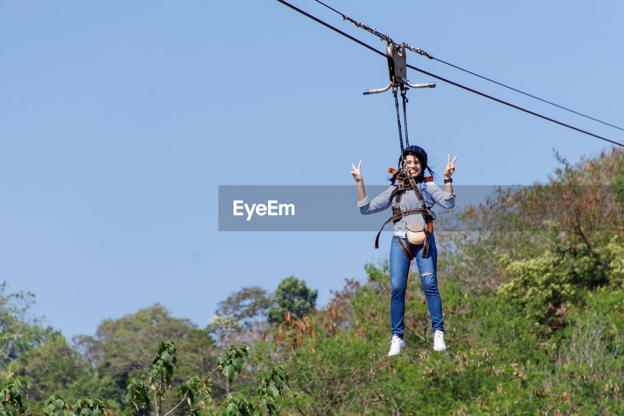 Portrait of woman hanging from safety harness while rappelling against sky