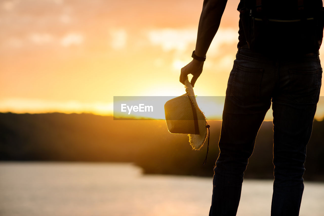 MAN HOLDING UMBRELLA AGAINST SKY AT SUNSET