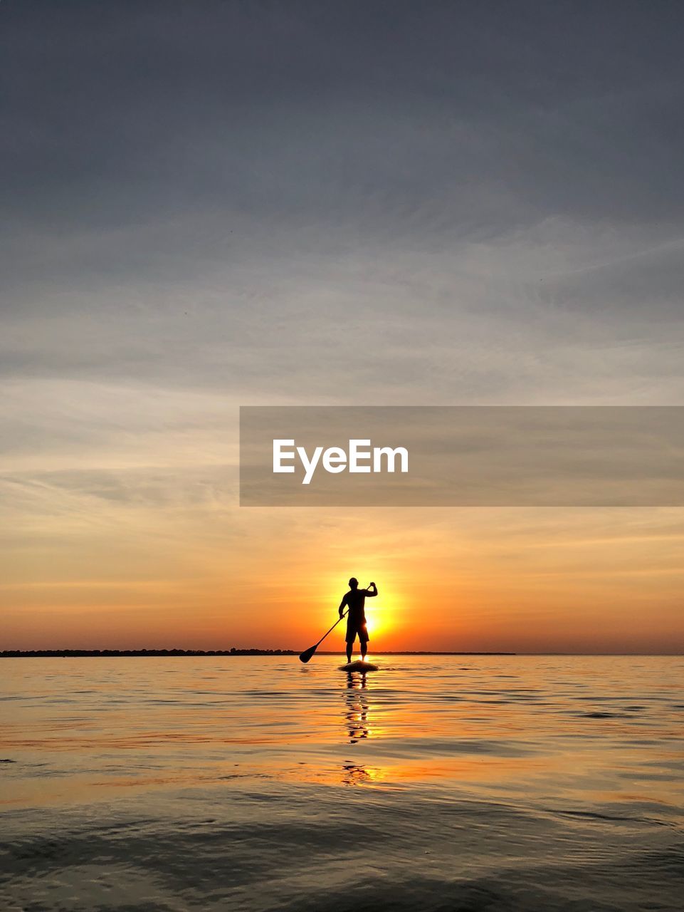 Silhouette of man paddleboarding on sea against sky during sunset