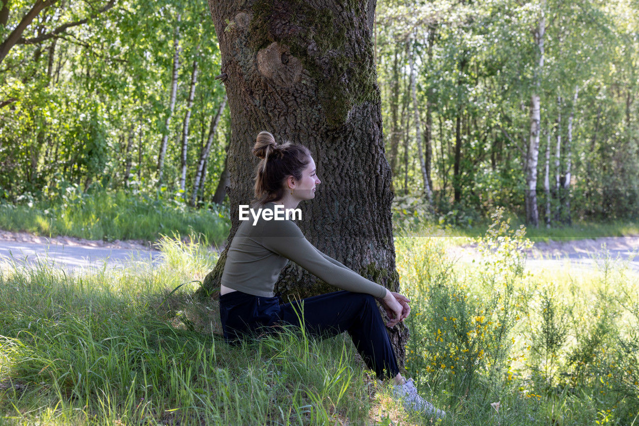 side view of young woman looking away while standing in forest
