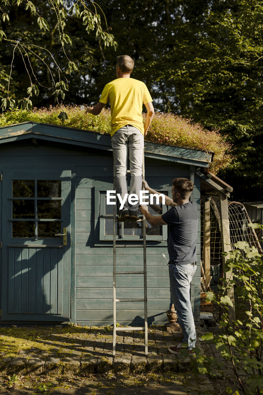 Father standing on ladder being supported by son in front of house