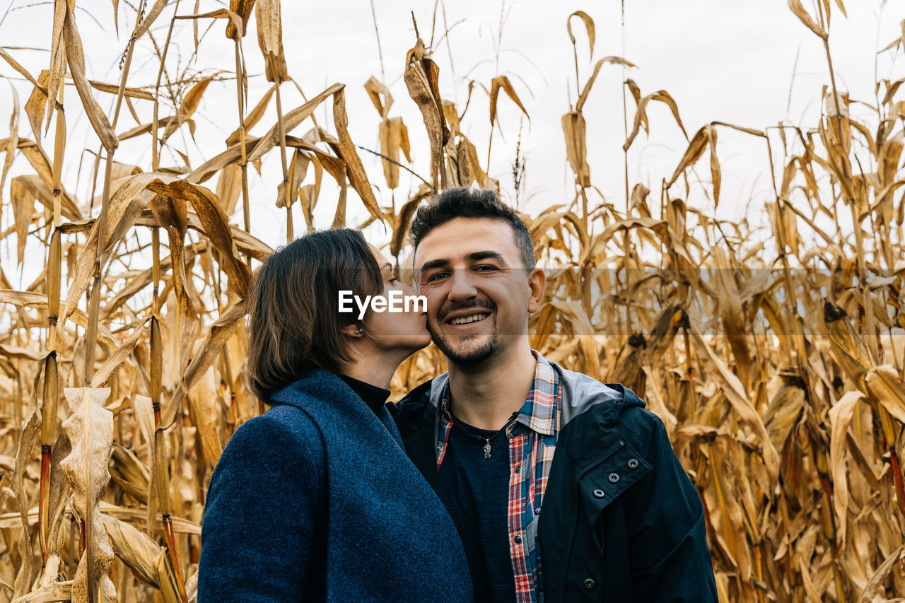 Woman kissing happy smiling man on the cheek standing in autumn in a cornfield