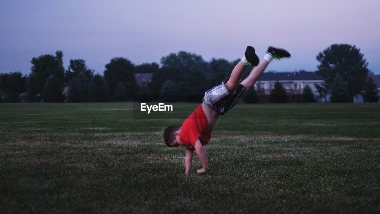 Full length of boy performing handstand on grassy field against sky