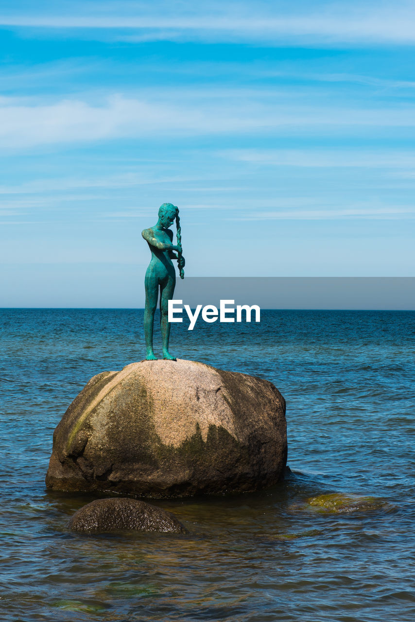 MAN ON ROCK IN SEA AGAINST SKY