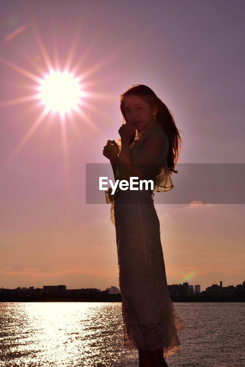 WOMAN STANDING AT SEA DURING SUNSET