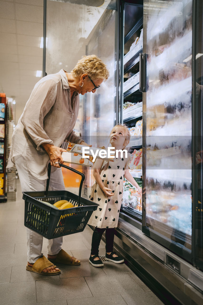 Senior woman holding basket while buying groceries with granddaughter at store