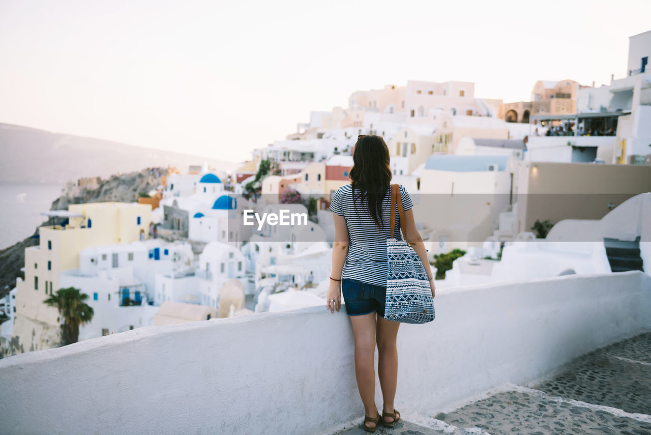 Greece, santorini, oia, back view of woman looking to the village at evening twilight