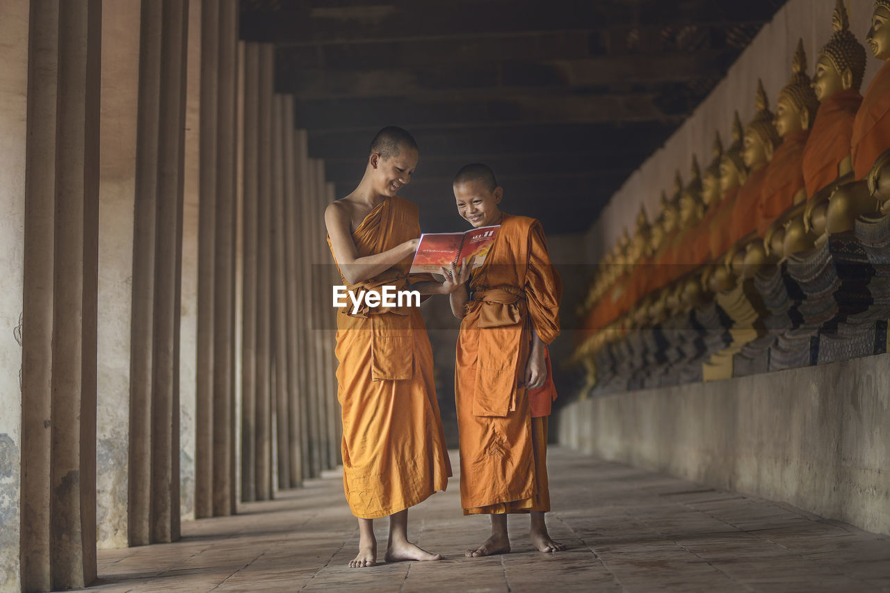 Monks smiling while reading book in corridor