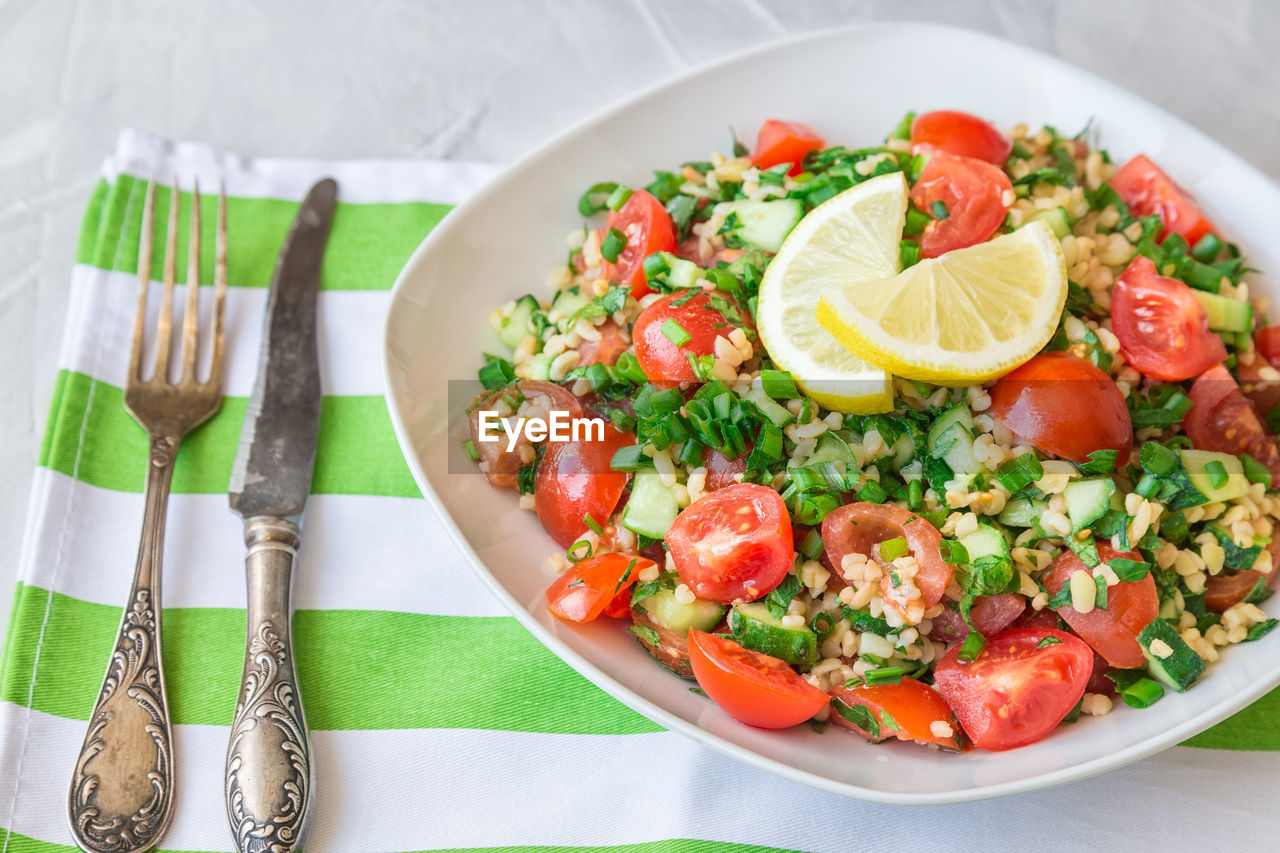 Tabbouleh salad on a dish on light gray concrete background. healthy vegetarian food.