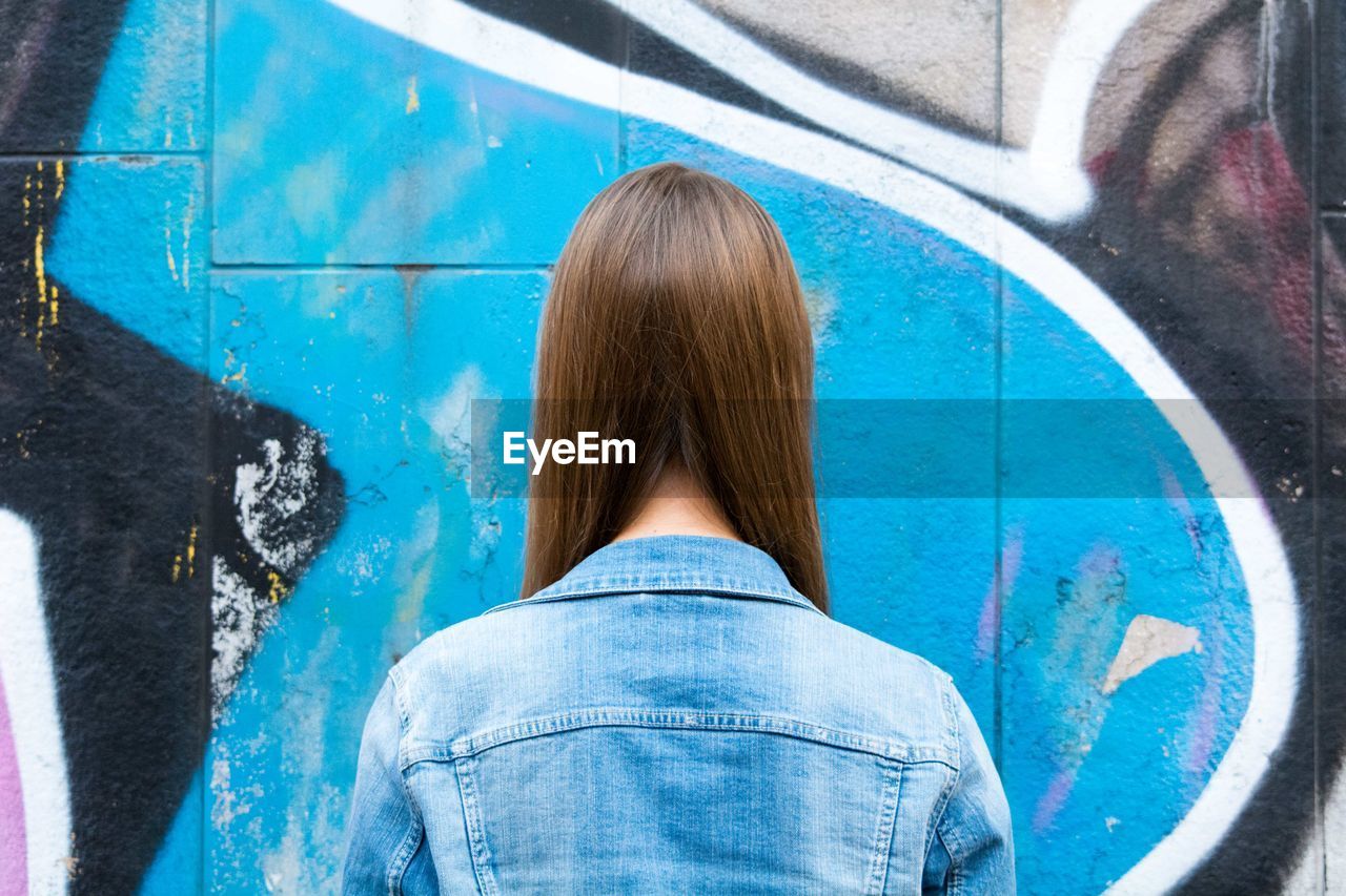 Rear view of woman against wall with graffiti