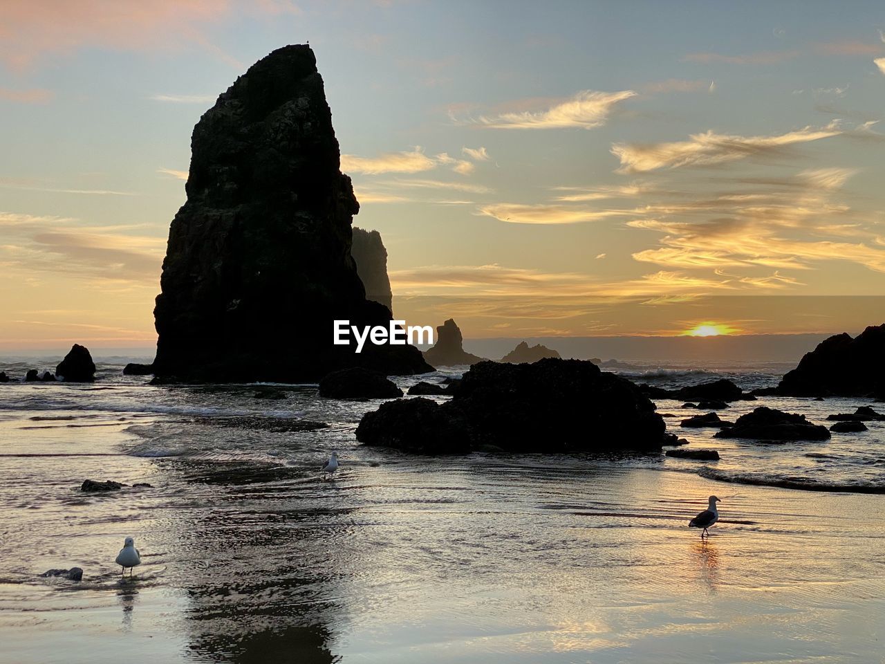 Rocks on sea shore against sky during sunset