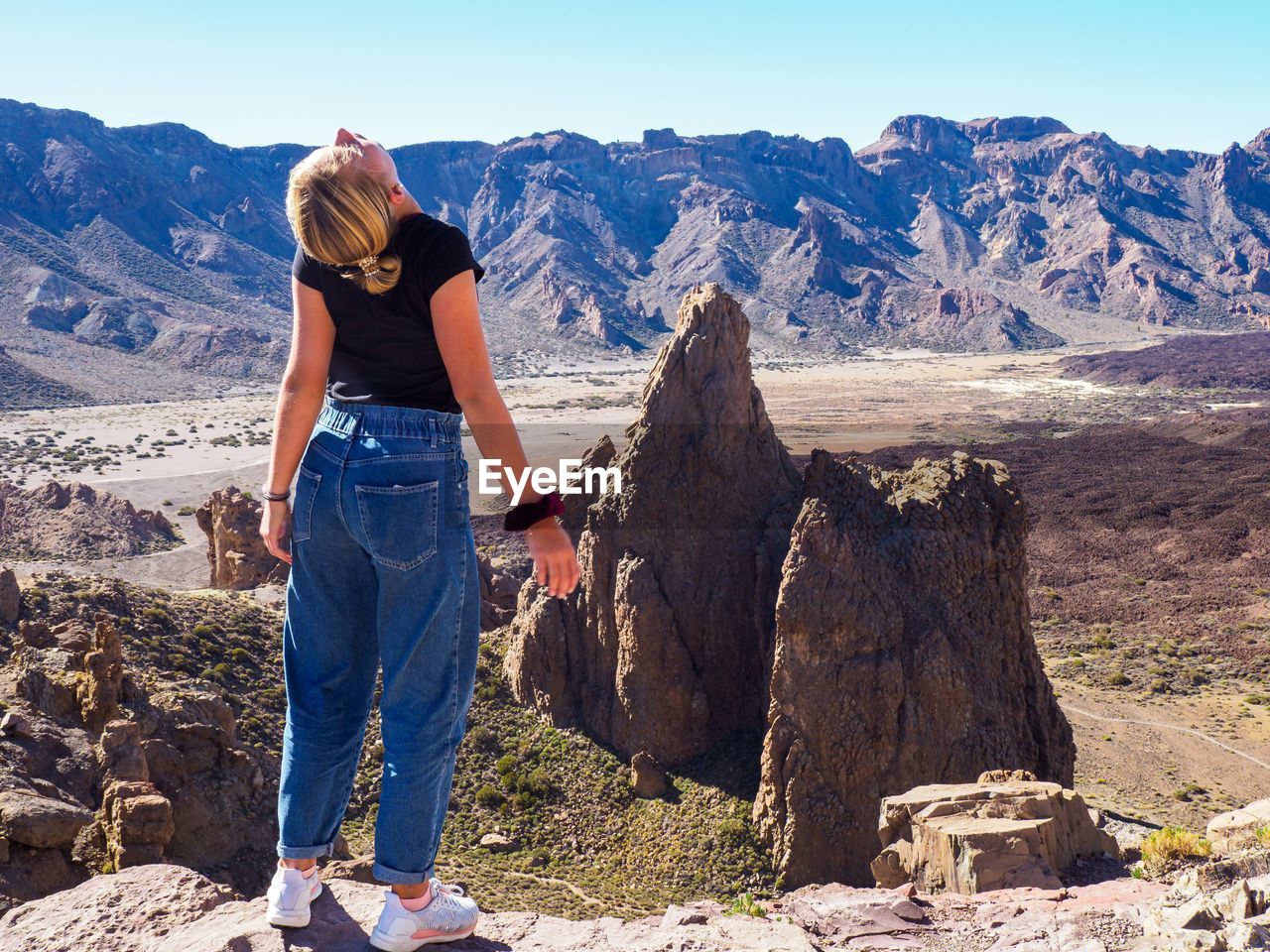 Rear view of girl stretching neck while standing on mountain