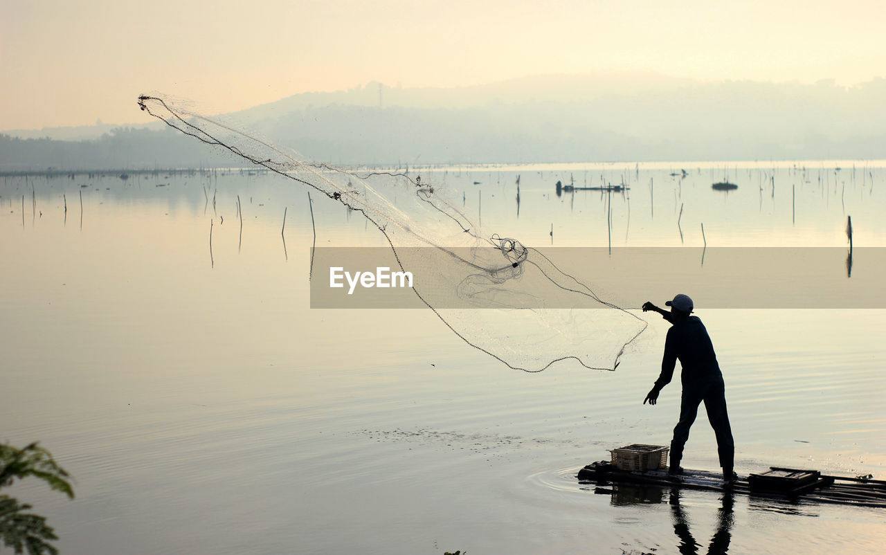 Man fishing in lake against sky