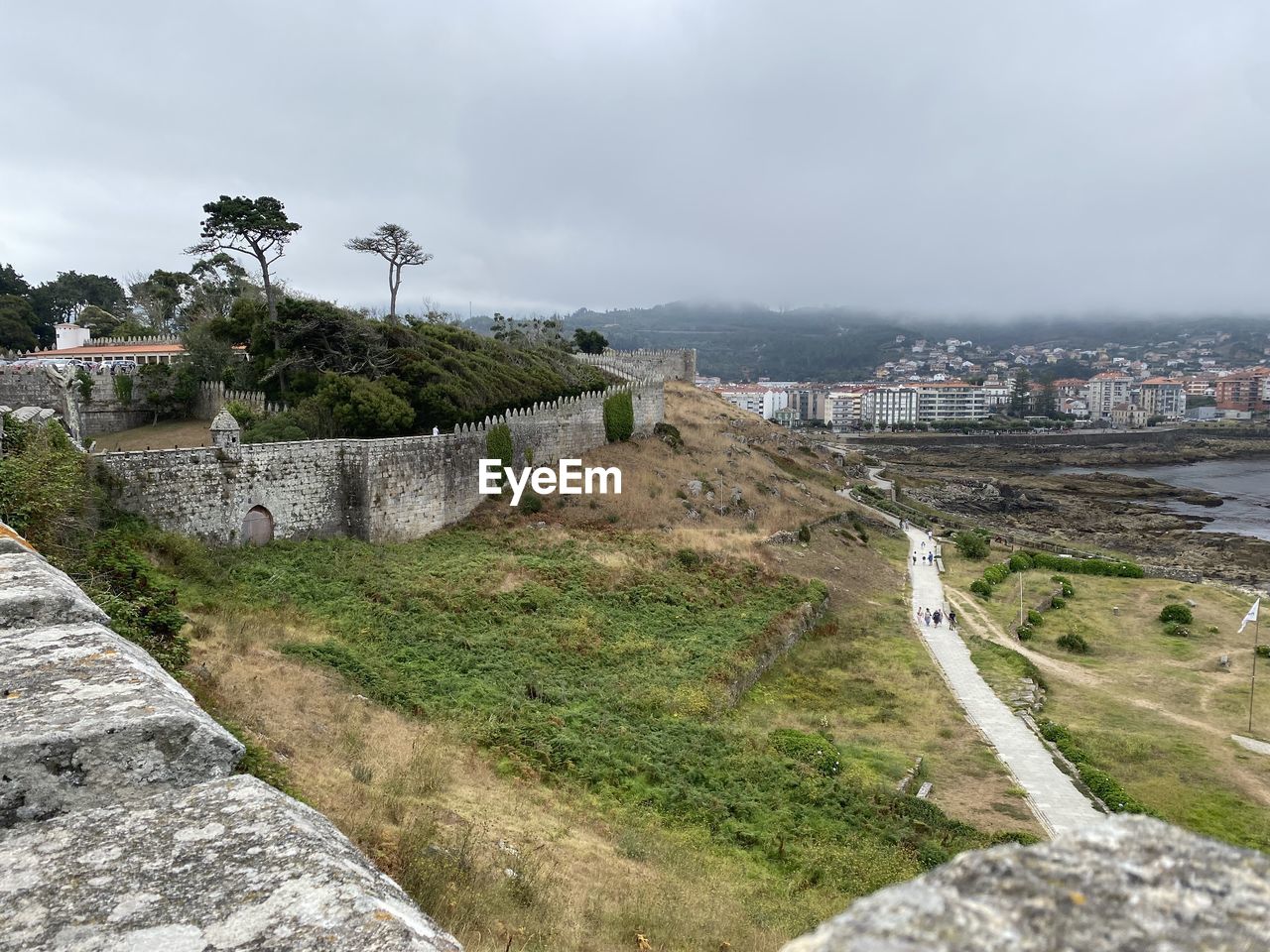 architecture, built structure, coast, sky, building exterior, sea, nature, travel destinations, cloud, water, city, building, travel, environment, land, tourism, history, landscape, plant, the past, no people, tree, terrain, cliff, cityscape, ruins, outdoors, overcast, beach, scenics - nature, wall, day, high angle view, beauty in nature, coastline, fortification, hill, holiday, shore, street, vacation, trip, town, house, road, residential district, rock, fog