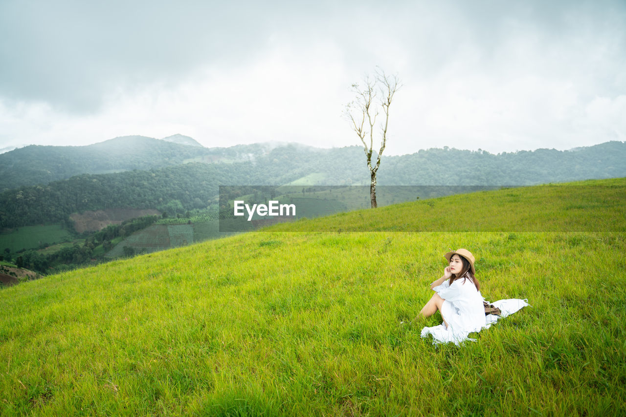 WOMAN SITTING ON GRASSY FIELD