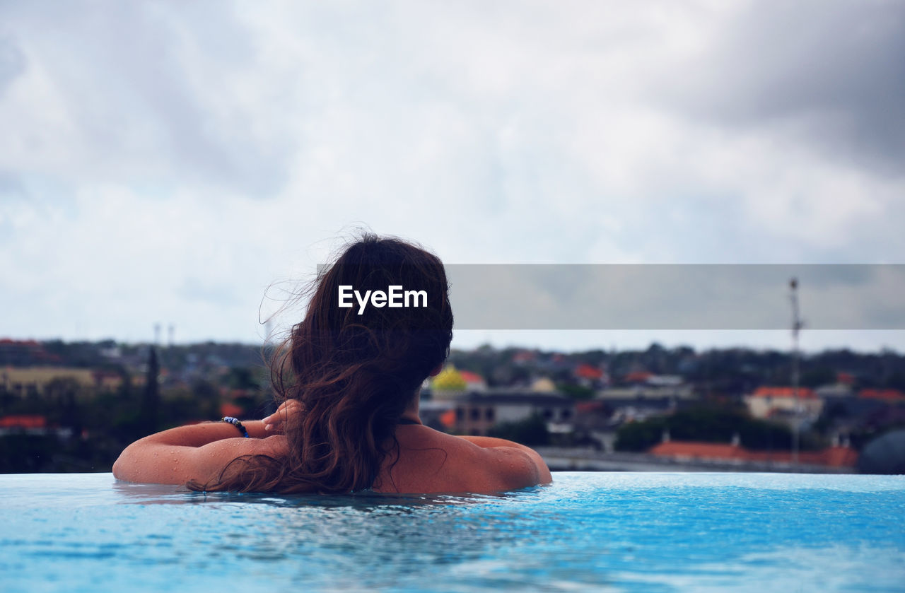 Rear view of woman swimming in infinity pool against sky