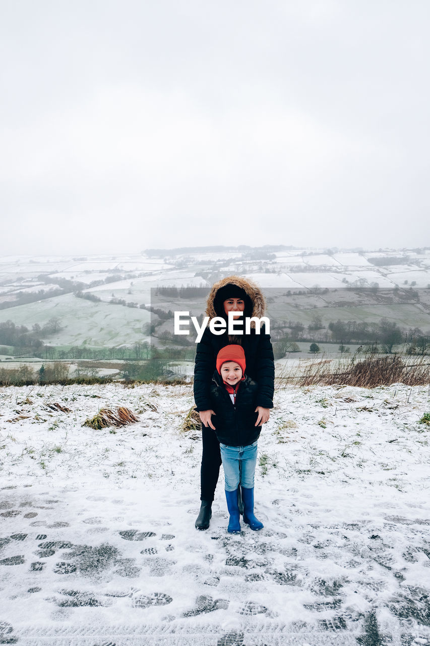 Portrait of cute boy with mother standing on snow covered mountain road at winter