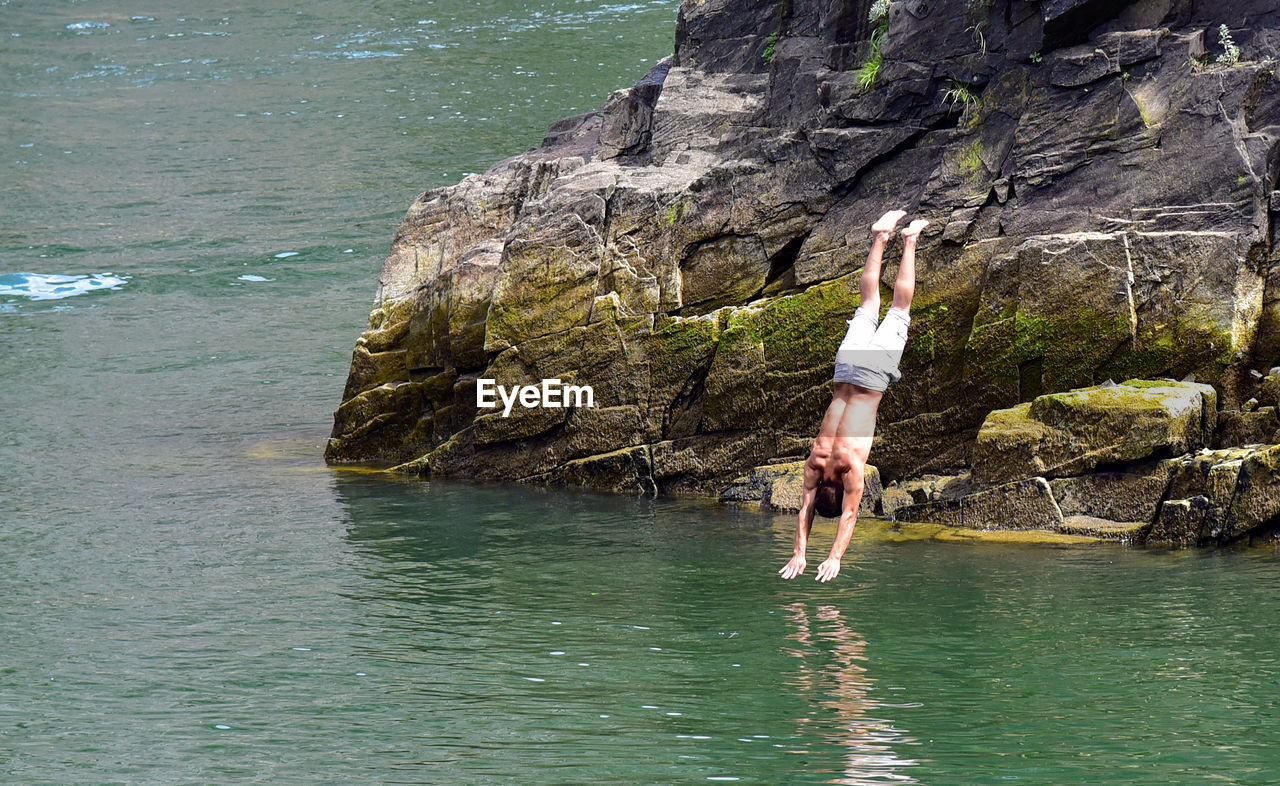 Man jumping from rock at sea