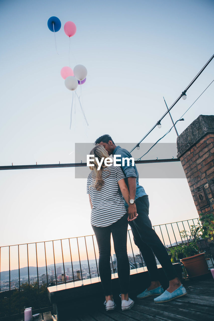 Couple standing with balloons against sky