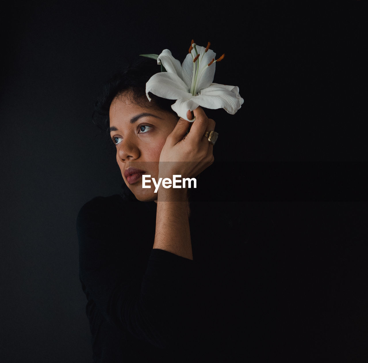 Thoughtful woman wearing flower against black background