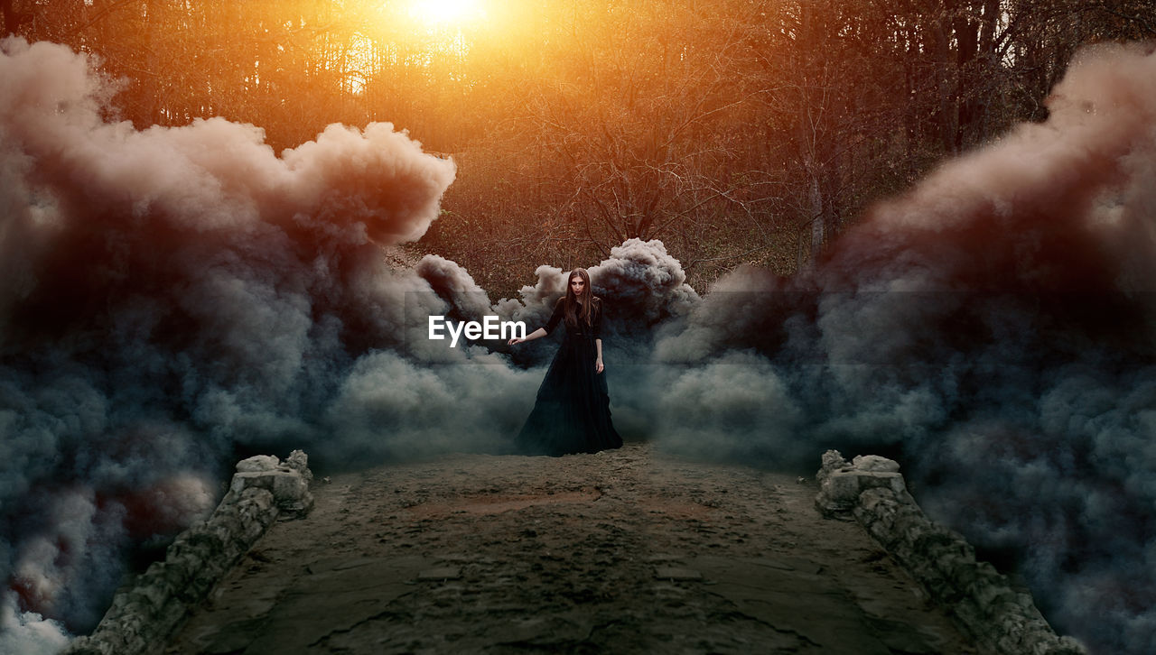 Digital composite image of woman wearing dress while standing in forest amidst smoke