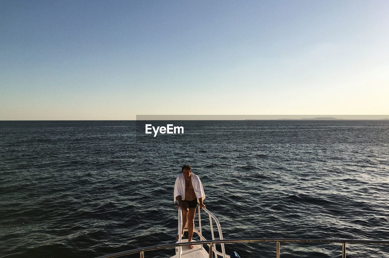 Full length of man standing on boat in sea against clear sky during sunset