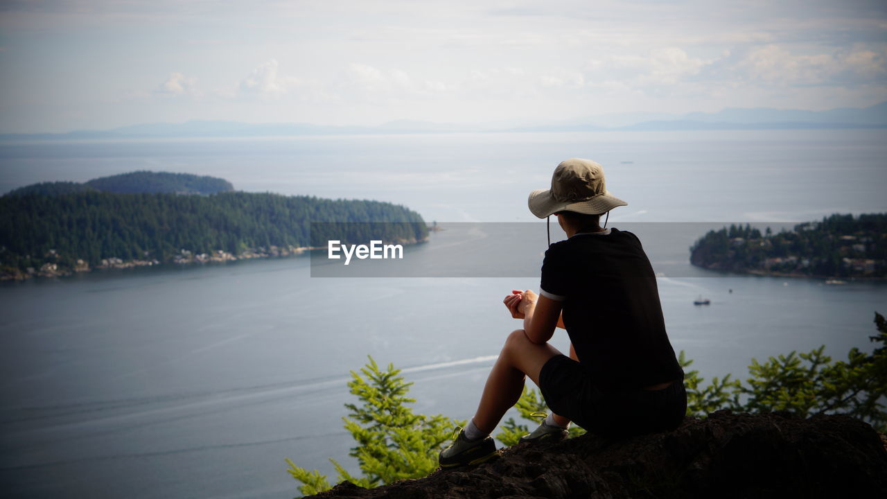 Side-back view of woman looking at the ocean and the land in front of her, under a covered sky