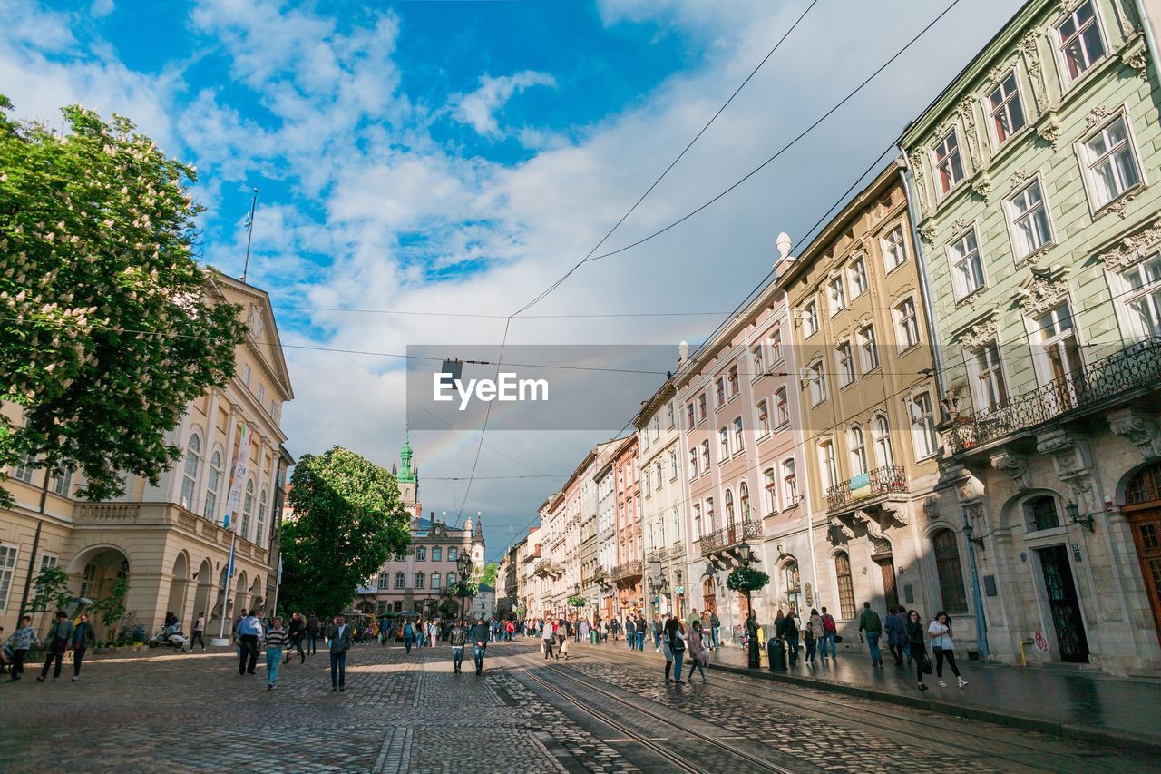 People walking in city against cloudy sky