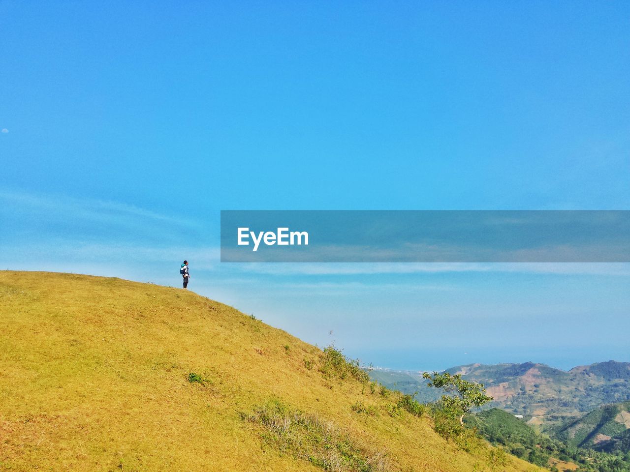 Mid distance view of man standing on mountain against blue sky