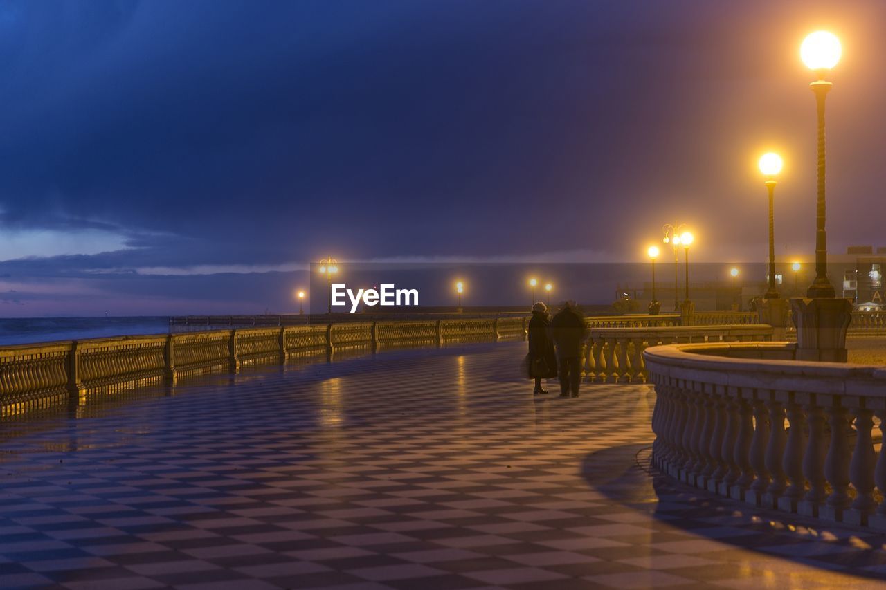 MAN AT ILLUMINATED BEACH AGAINST SKY AT NIGHT