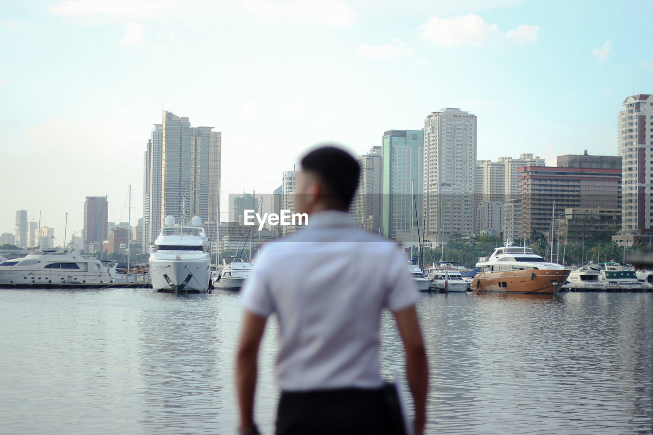 REAR VIEW OF MAN STANDING BY BUILDINGS AGAINST SKY