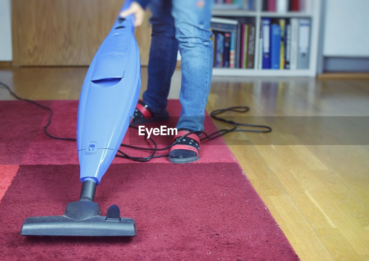 Low section of person cleaning floor with at vacuum cleaner at home