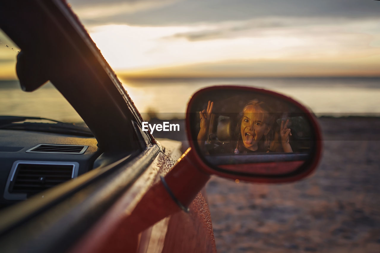 Reflection of girl making face seen in side-view mirror