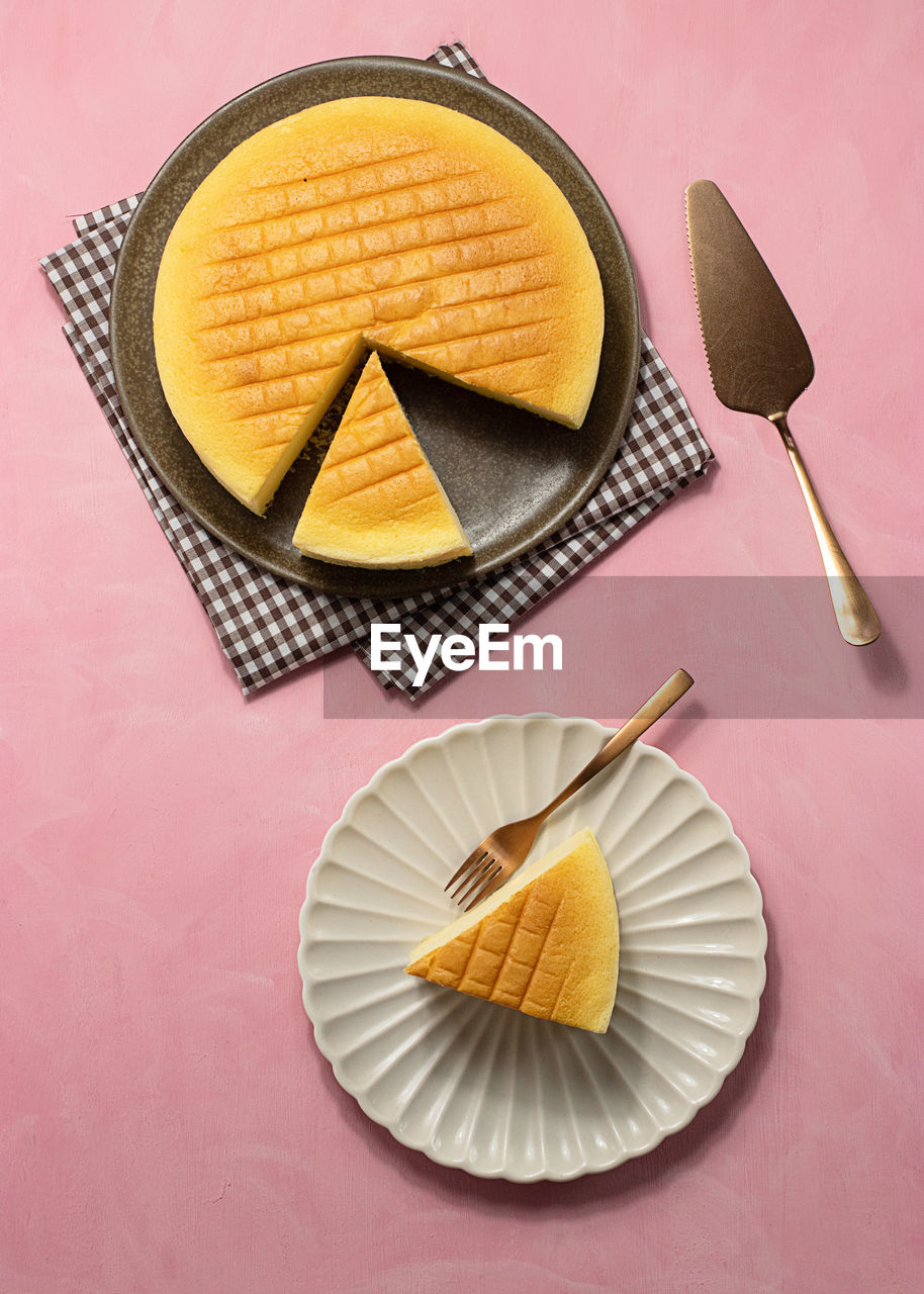 Top view of delicious cotton cheesecake served on plates near napkin and spatula on pink background