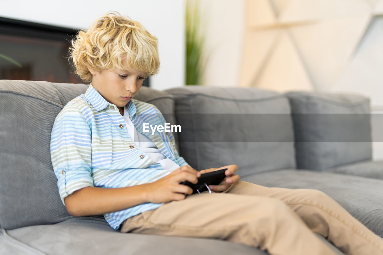 Boy using mobile phone while sitting on sofa