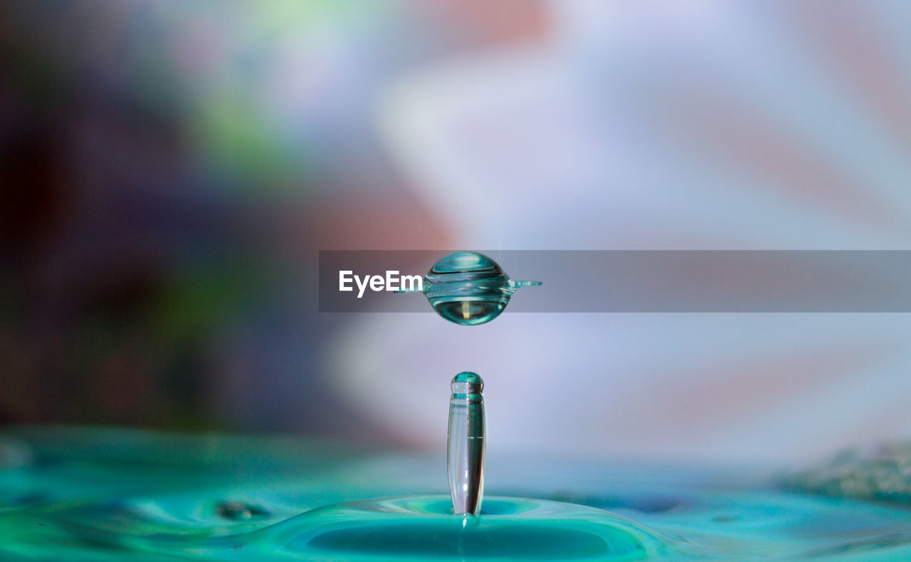 Close-up of blue drop falling in water against gray background