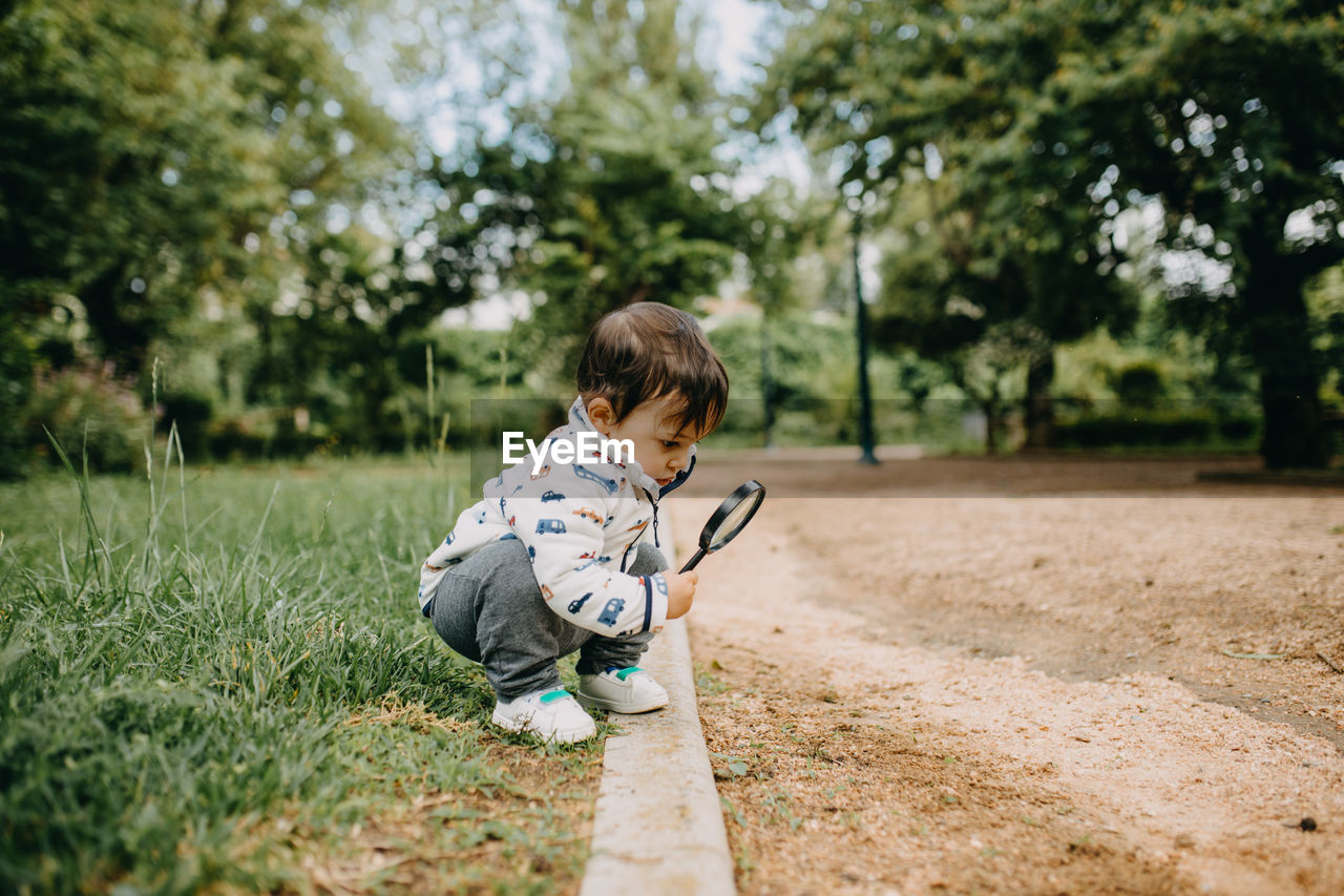 Full length of boy using magnifying glass outdoors