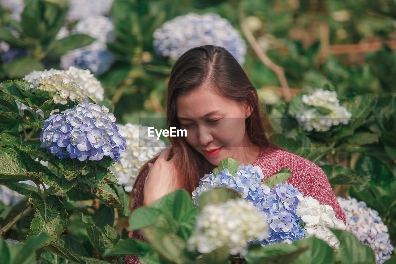 PORTRAIT OF WOMAN WITH PINK FLOWERS AGAINST PLANTS