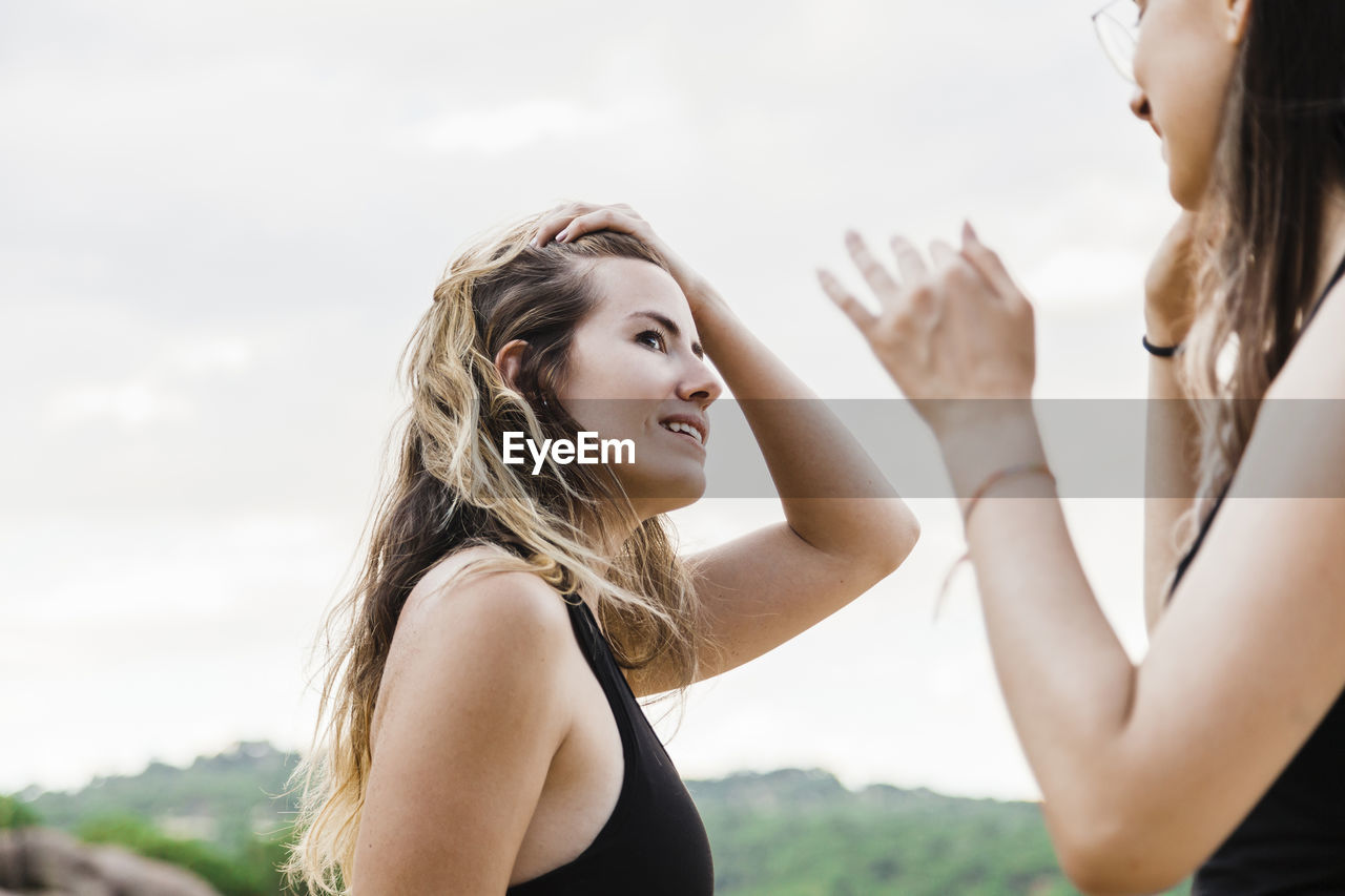 Beautiful young woman with hand in hair looking at female friend