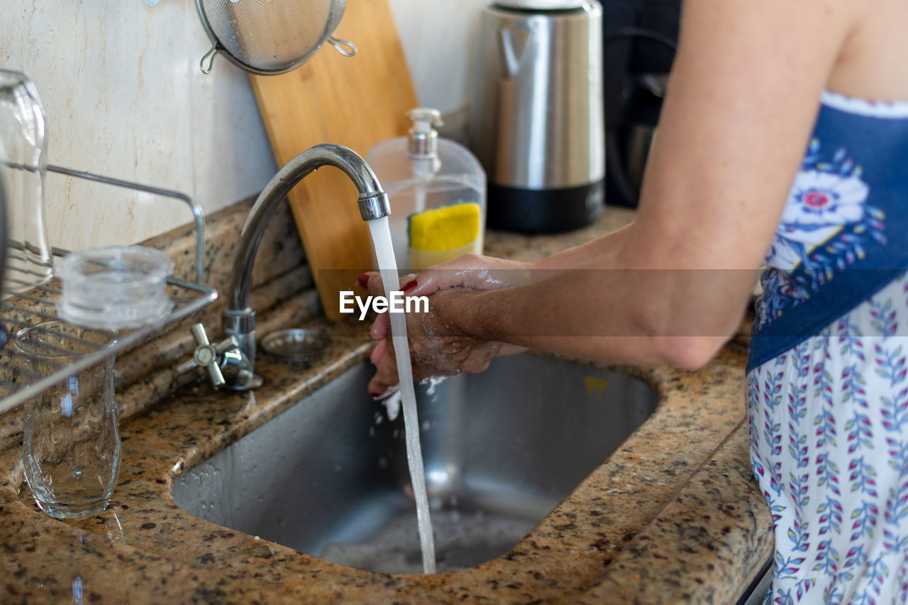 A woman, in the kitchen, washing her hands thoroughly before cooking. healthy eating