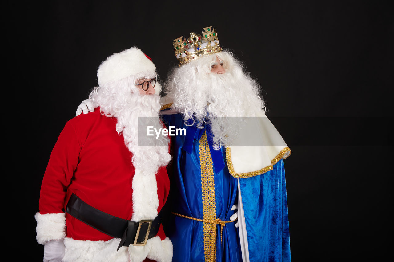 Rey mago and santa claus hugging as friends on a black background