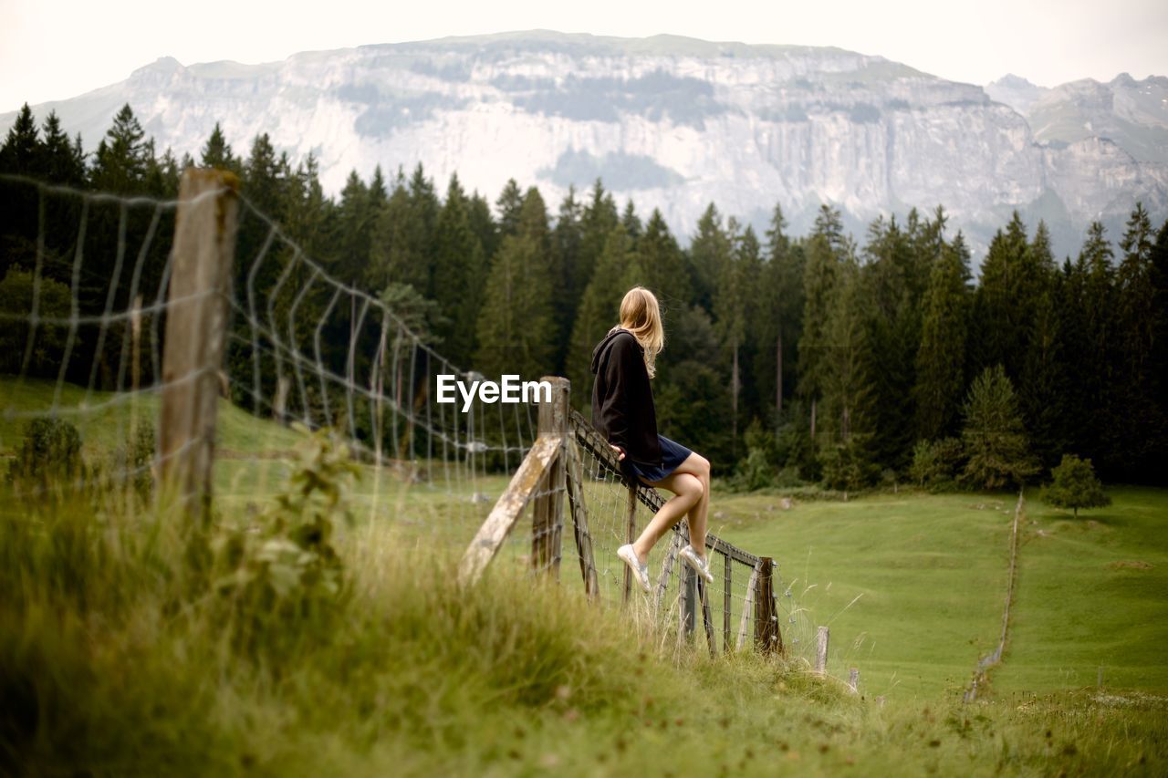 Full length of woman sitting on fence over field