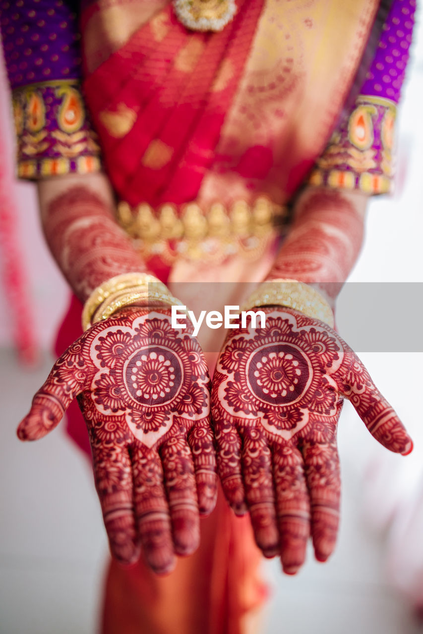 Midsection of bride wearing sari and jewelry while showing henna tattoo