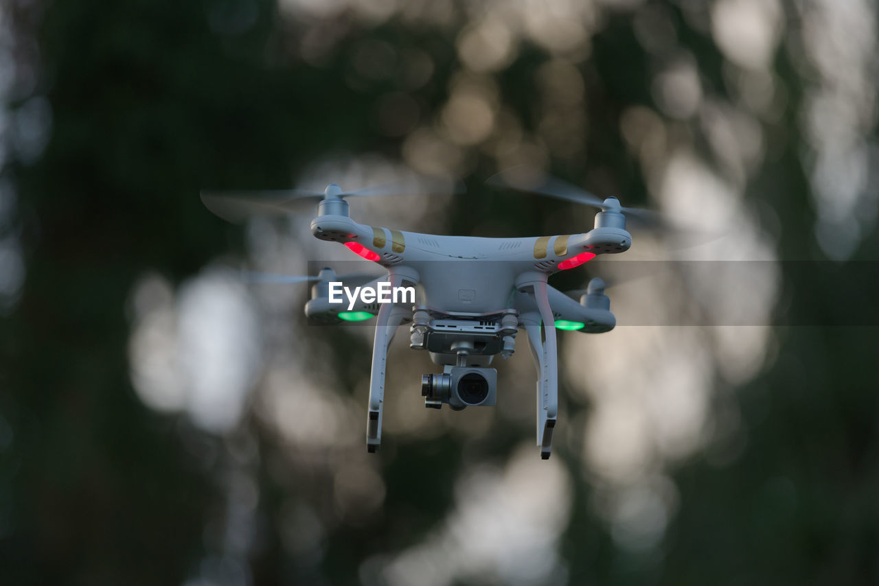 Drone quadcopter hovering in front of trees, blurred background of defocused trees at sunset
