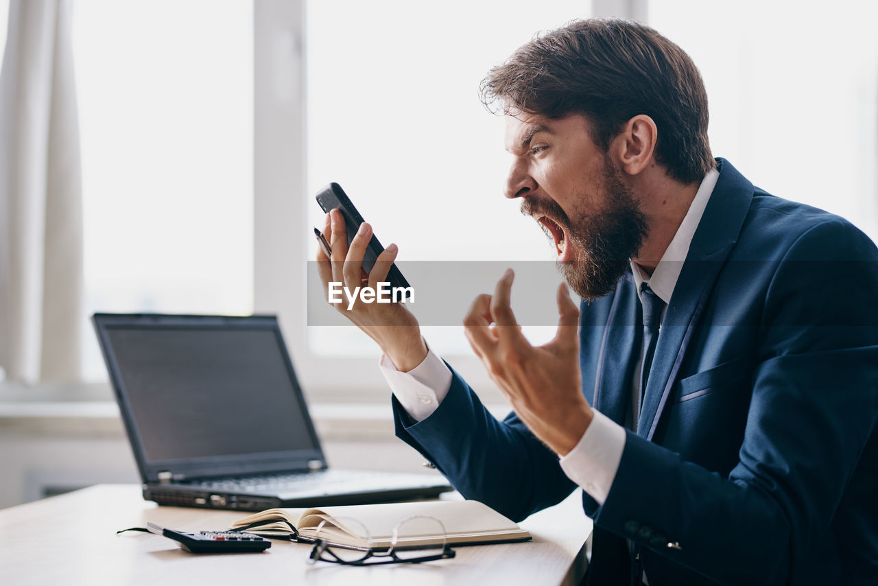 Angry businessman shouting on phone at office