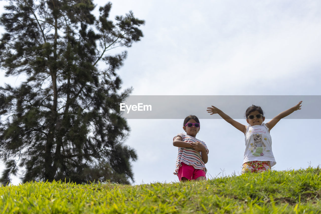 Low angle view of sisters playing on grass against sky