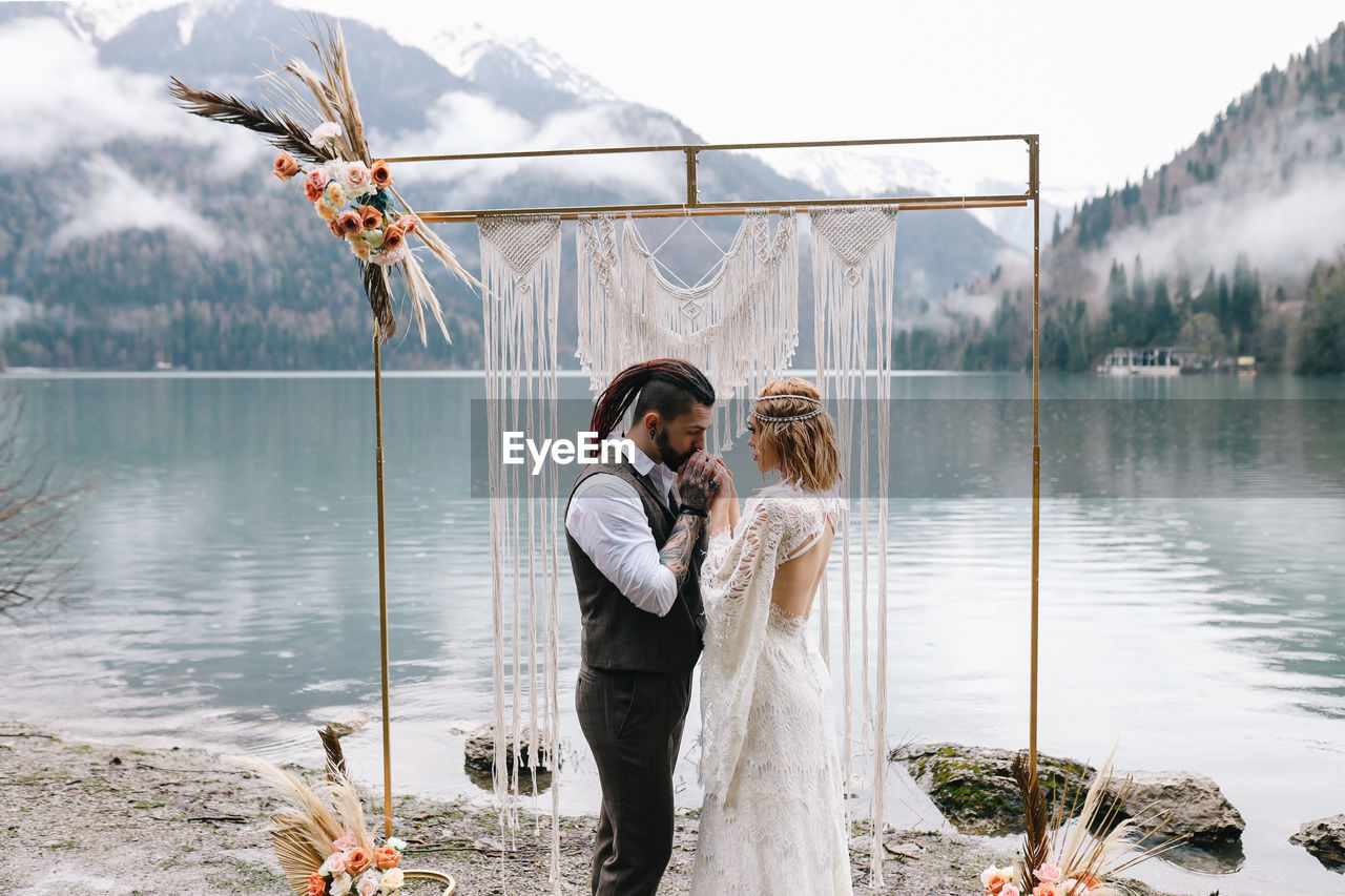 Happy newlyweds in love a man and a woman in wedding clothes embrace on the shore of the lake