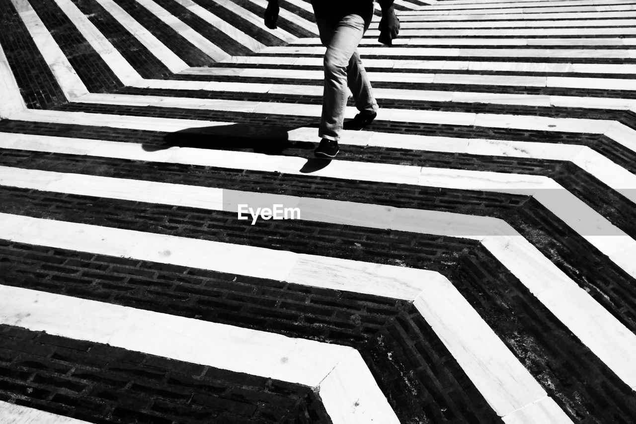 Low section of person walking on striped on footpath during sunny day